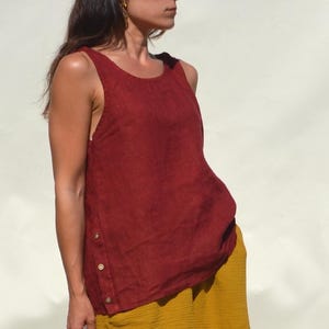 Könnte beinhalten: Ein ärmelloses, weinrotes Oberteil mit rundem Ausschnitt und seitlichem Knopfverschluss. Das Oberteil wird mit einem senfgelben Rock kombiniert. Das Outfit besteht aus einem leichten Stoff, der für warmes Wetter geeignet ist.