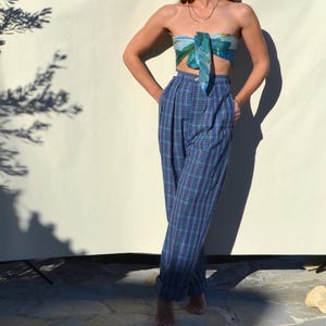 May include: Blue plaid high-waisted pants with a matching scarf top. The pants have a wide leg and a pleated front. The scarf top is tied in a knot at the front. The outfit is worn with bare feet.