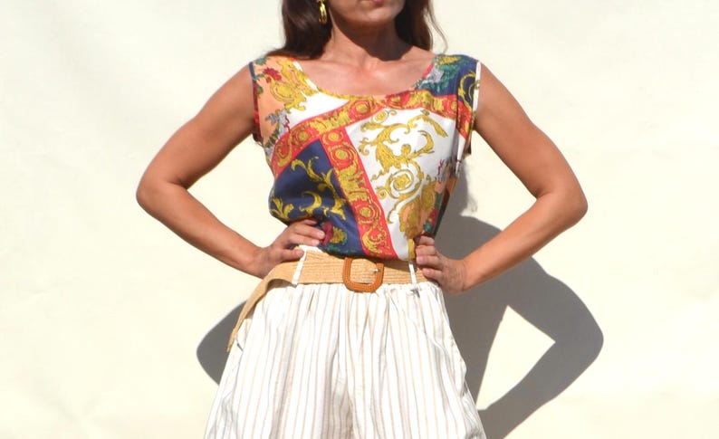 Pode incluir: Um top sem mangas com uma estampa barroca colorida em tons de azul, vermelho, dourado e branco. O top &eacute; combinado com um cinto tecido bege e cal&ccedil;&otilde;es listrados brancos. O conjunto &eacute; de estilo vintage.
