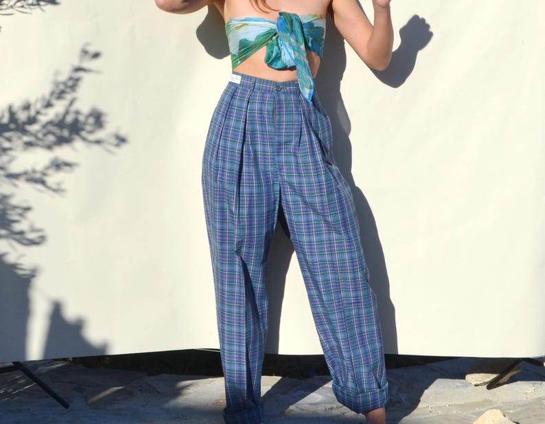 May include: Blue plaid high-waisted pants with pleats. The pants have a relaxed fit and are cuffed at the ankles. A silk scarf in shades of blue and green is worn as a top.