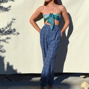 May include: A woman's outfit featuring high-waisted, blue plaid pants and a matching scarf top. The pants have a relaxed fit and are cuffed at the ankles. The scarf top is tied in a bandeau style, with a blue and green pattern.
