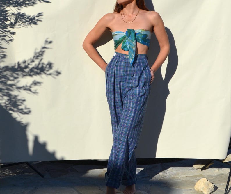 May include: A woman's outfit featuring high-waisted, blue plaid pants and a matching scarf top. The pants have a relaxed fit and are cuffed at the ankles. The scarf top is tied in a bandeau style, with a blue and green pattern.