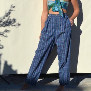 May include: Blue plaid high-waisted pants with pleats. The pants have a straight leg and a button closure. The plaid pattern includes shades of blue, green, and purple. The pants are made of a lightweight fabric.