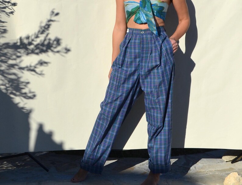 May include: Blue plaid high-waisted pants with pleats. The pants have a straight leg and a button closure. The plaid pattern includes shades of blue, green, and purple. The pants are made of a lightweight fabric.