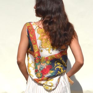 Pode incluir: Um top sem mangas com um padr&atilde;o ornamentado colorido com detalhes em vermelho, dourado e azul. O top &eacute; combinado com uma saia listrada branca e clara. O estilo geral sugere uma est&eacute;tica vintage ou retr&ocirc;.