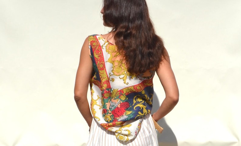 Pode incluir: Um top sem mangas com um padr&atilde;o ornamentado colorido com detalhes em vermelho, dourado e azul. O top &eacute; combinado com uma saia listrada branca e clara. O estilo geral sugere uma est&eacute;tica vintage ou retr&ocirc;.