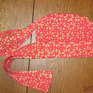 May include: A red and white patterned fabric headband with a tie. The headband is made of a soft, lightweight fabric and has a floral design.
