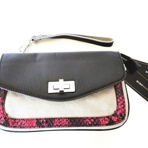 Może przedstawiać: Czarna i biała kopertówka z paskiem na nadgarstek. Kopertówka posiada czarną skórzaną klapę ze srebrnym zapięciem. Dolna część wykonana jest z jasnego płótna z różowym wykończeniem wężowym.