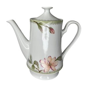 Puede incluir: Una taza de cerámica blanca con un asa negra y el texto "But First, Coffee" en negrita negra. La taza se encuentra sobre un fondo neutro, resaltando su diseño simple.