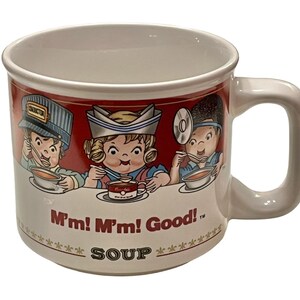 May include: White ceramic mug with a red band featuring cartoon characters eating soup. The mug has the text "M'm! M'm! Good!" and "SOUP" printed on it. The mug has a large, curved handle.