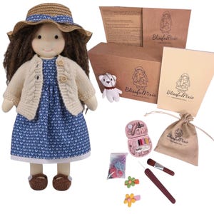 May include: A handmade fabric doll with brown hair, wearing a straw hat, a cream-colored knit cardigan, and a blue patterned dress with brown shoes. Included are a small bear keychain, a sewing kit, a drawstring bag, and hair accessories.