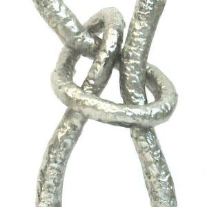 Puede incluir: Una escultura de metal plateado de un nudo infinito, montada sobre una base rectangular negra. El nudo tiene una superficie texturizada y un diseño moderno y abstracto, adecuado para la decoración del hogar.