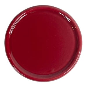 May include: A circular, deep red ceramic plate with a smooth, glossy finish. The plate features a slightly raised, rounded rim that frames the flat, solid-coloured centre. The surface reflects light evenly, highlighting the vibrant, uniform red hue.