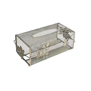 Puede incluir: Un porta-cajas de pañuelos de malla metálica rectangular con adornos florales. El soporte es de color dorado apagado y presenta flores decorativas en la parte delantera y los laterales. La parte superior tiene una abertura rectangular.