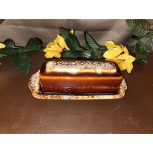 May include: A rectangular ceramic butter dish featuring a glossy dark brown glaze with a textured, cream-coloured drip pattern along the top edge and the base rim. The dish consists of a lidded container and a matching rectangular tray with handles.