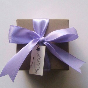 May include: A small, brown gift box tied with a lavender satin ribbon and bow. A white tag with the text "Mikelita Zen" is attached to the ribbon.
