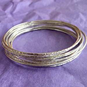 May include: A set of silver bangles with a hammered texture. The bangles are stacked on top of each other, creating a layered look.