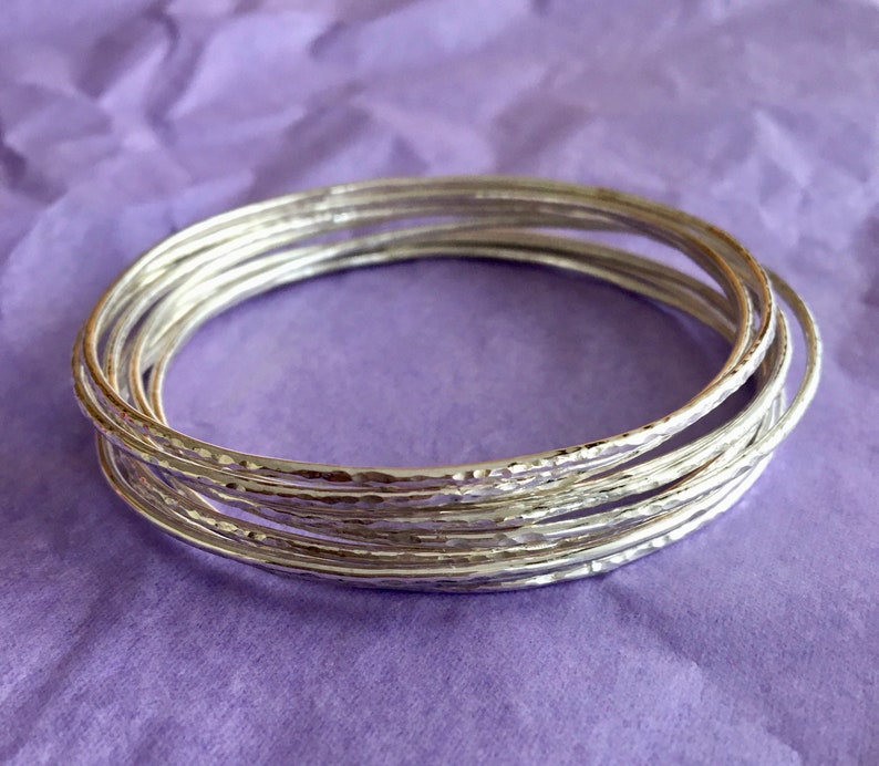 May include: A set of silver bangles with a hammered texture. The bangles are stacked on top of each other, creating a layered look.