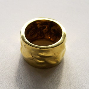May include: A gold ring with a textured surface. The ring is thick and has a wide band.