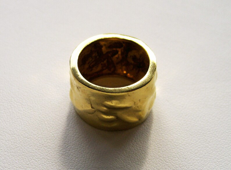 May include: A gold ring with a textured surface. The ring is thick and has a wide band.