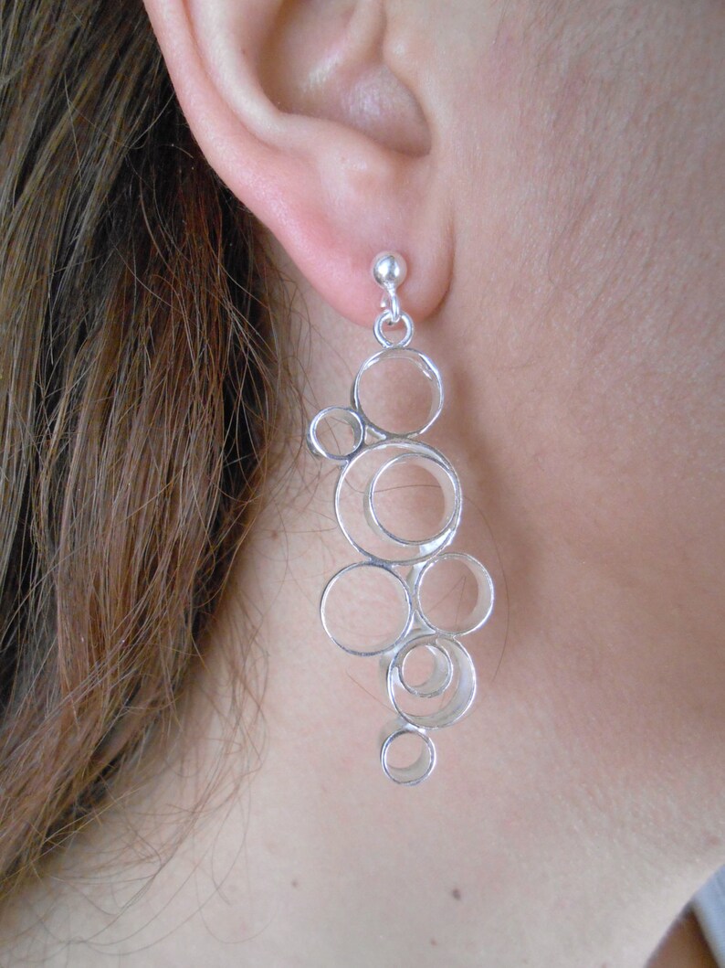 May include: Silver dangle earrings with a design of multiple interconnected circles.