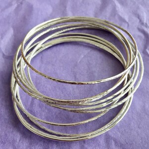 May include: A set of silver bangles with a hammered texture. The bangles are stacked on top of each other, creating a layered look.