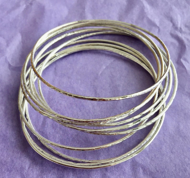 May include: A set of silver bangles with a hammered texture. The bangles are stacked on top of each other, creating a layered look.