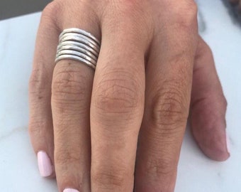 Könnte beinhalten: Eine Hand mit einem Stapel silberner Ringe. Die Nägel sind in einem hellen Rosaton lackiert.
