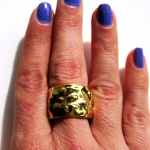 May include: A gold ring with a textured surface on a hand with blue nail polish.