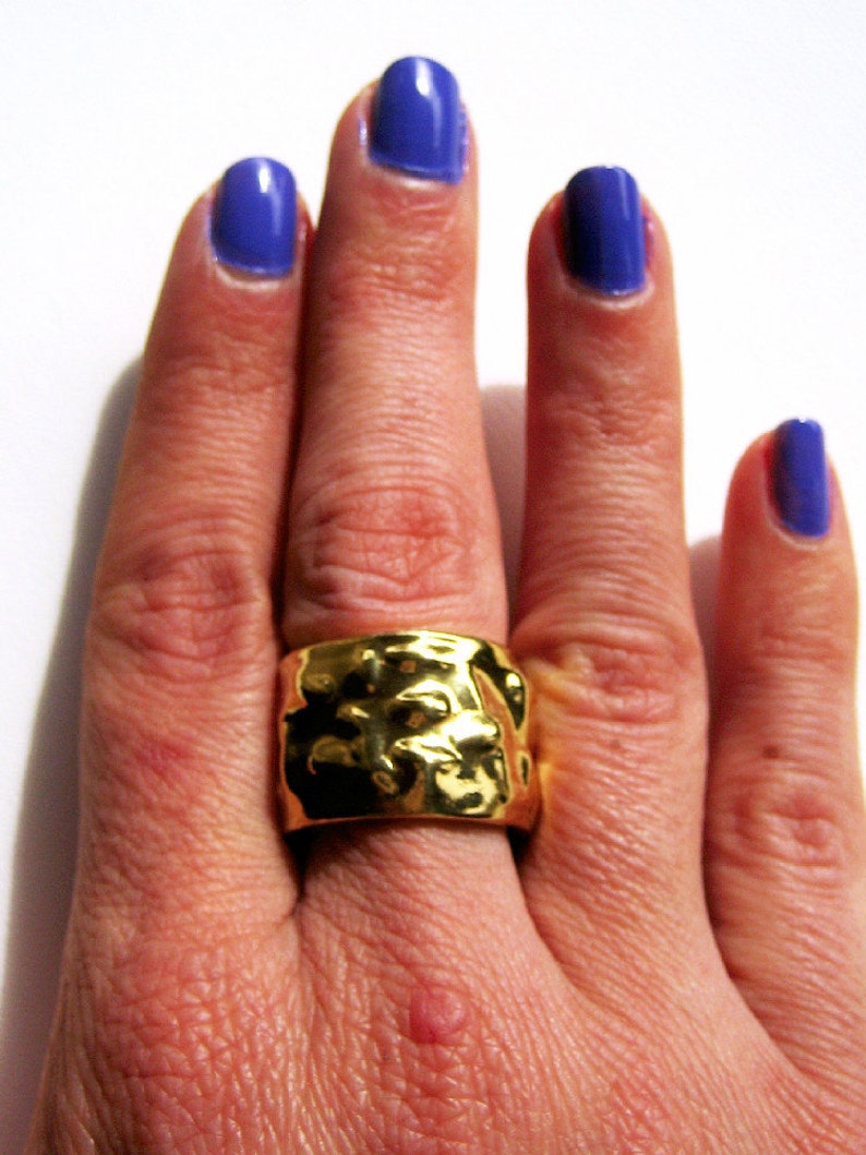 May include: A gold ring with a textured surface on a hand with blue nail polish.