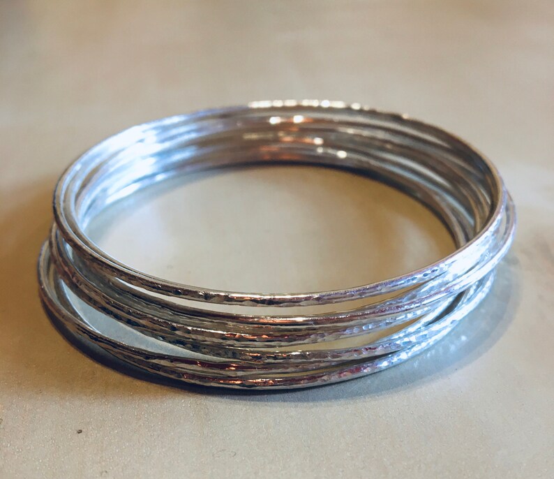 May include: A set of silver bangles with a hammered texture. The bangles are stacked on top of each other.