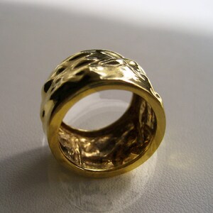 May include: A gold ring with a textured, hammered finish. The ring is wide and has a rounded shape.