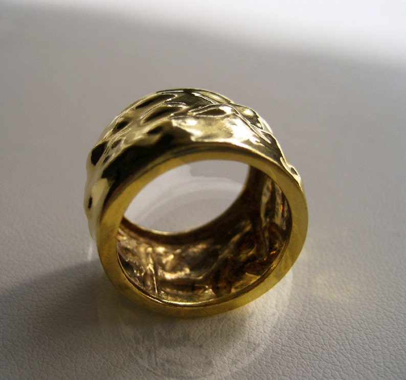 May include: A gold ring with a textured, hammered finish. The ring is wide and has a rounded shape.