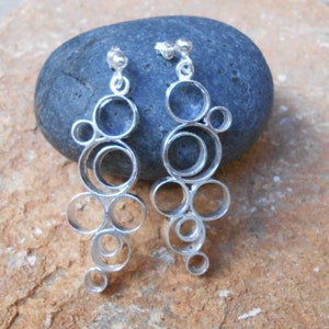 May include: A pair of silver dangle earrings with a design of multiple interconnected circles.