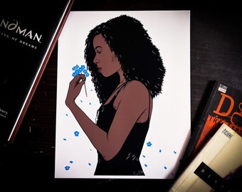 May include: Comic book style illustration of a woman with dark hair and a black dress holding blue flowers. The artwork has a white background with blue flower accents. Two books are visible in the background.