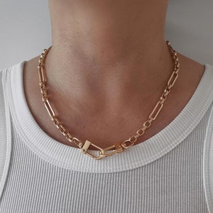 May include: A gold chain necklace with a unique clasp design. The chain is made of linked rectangular and round metal pieces.