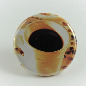 May include: A round button with a white background and a picture of a coffee cup with coffee in it. The coffee cup is surrounded by coffee beans.
