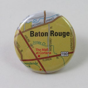 May include: A yellow and brown button with a map of Baton Rouge, Louisiana. The map shows the location of "The Mall at Cortana" and the highway number 190.