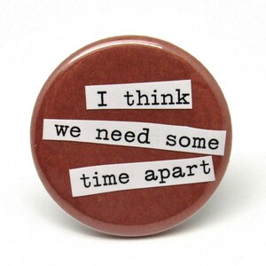 May include: A brown round button with white paper strips that say "I think we need some time apart".