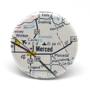 May include: A vintage-style map button featuring a close-up of the Merced, California area. The map shows roads, highways, and landmarks, including Yosemite National Park, Castle Air Force Base, and the city of Merced. The button is white with black and blue text and lines.