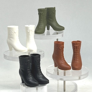 May include: A collection of miniature, heeled boots in various colors: white, olive green, brown, and black. Each boot features a lace-up design and decorative floral accents. The boots are displayed on clear, tiered platforms.