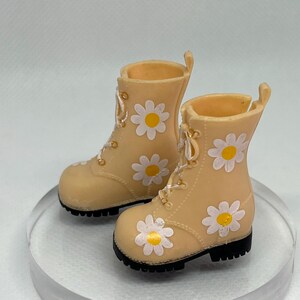 May include: A pair of beige ankle boots with white daisy print and black soles.