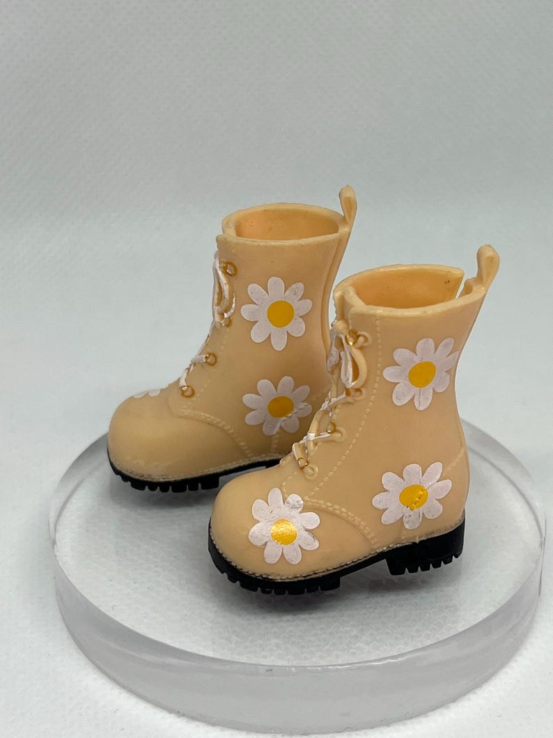 May include: A pair of beige ankle boots with white daisy print and black soles.
