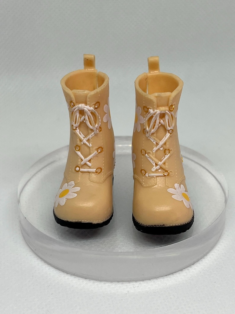 May include: A pair of beige ankle boots with white daisy print and white laces. The boots have a black sole.