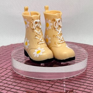 May include: A pair of beige lace-up boots with white daisy print. The boots have a white lace and gold accents.
