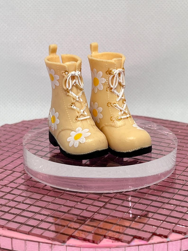 May include: A pair of beige lace-up boots with white daisy print. The boots have a white lace and gold accents.