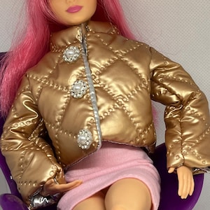 May include: A doll with pink hair and blue eyes wearing a gold quilted jacket with pearl-like buttons and a pink mini skirt. The doll is seated in a purple chair.