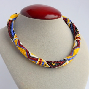 May include: A beaded necklace and bracelet set with a geometric pattern in yellow, red, blue, black, and white.