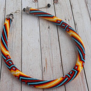 Op de afbeelding: Een kralenketting met een spiraalvormig ontwerp. De ketting heeft een patroon van rode, gele, blauwe en witte kralen. De ketting heeft een zilveren sluiting en ketting.