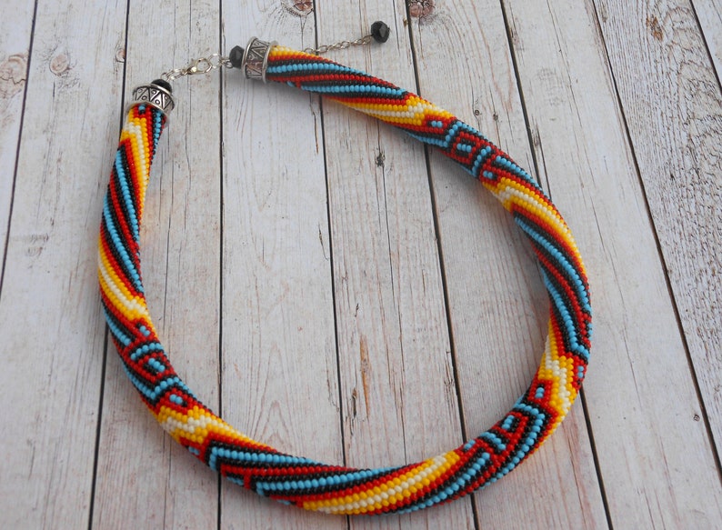 Op de afbeelding: Een kralenketting met een spiraalvormig ontwerp. De ketting heeft een patroon van rode, gele, blauwe en witte kralen. De ketting heeft een zilveren sluiting en ketting.